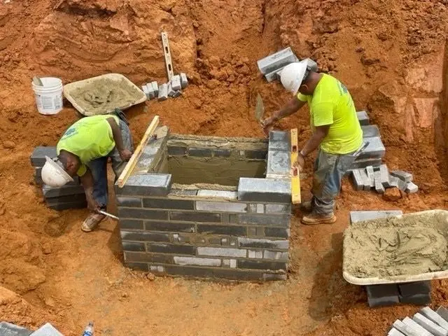 Crew constructing a masonry catch basin in an excavation